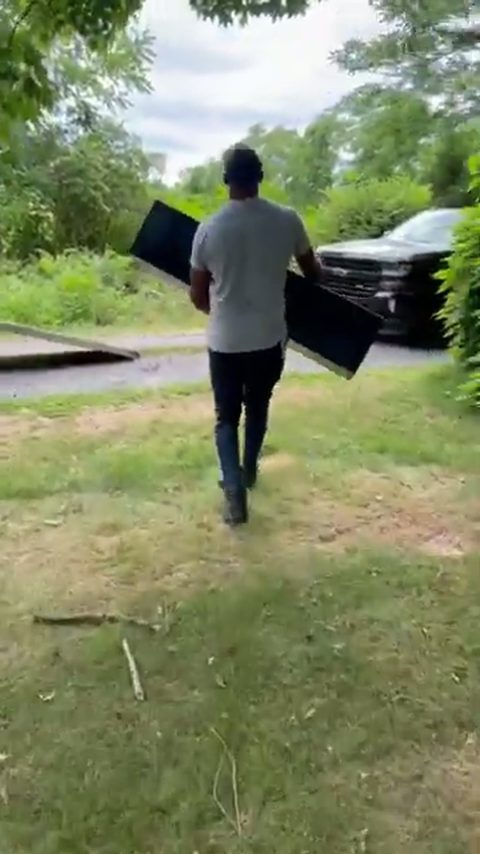 A strong mover carries a heavy gun safe across a yard toward a moving truck