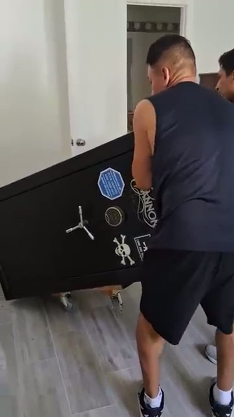 Two movers tilt a black Cannon gun safe onto a dolly inside a home prepped with floor protection