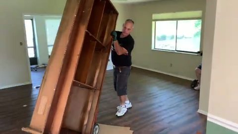 A mover tilts a tall wooden hutch onto a hand truck in an empty home