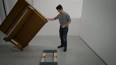A man tilts an upright piano onto a piano dolly by himself